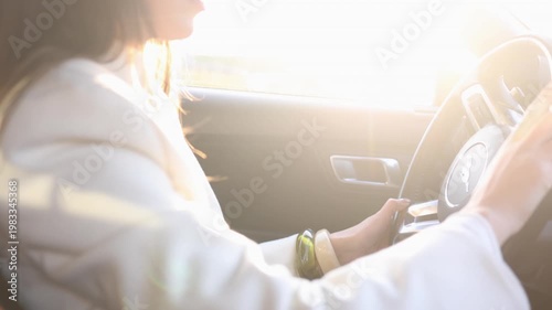 Side view of young woman in glasses and white jacket driving car in bright sunlight. Perfect for travel, road trip, freedom, lifestyle and transportation themed commercial projects