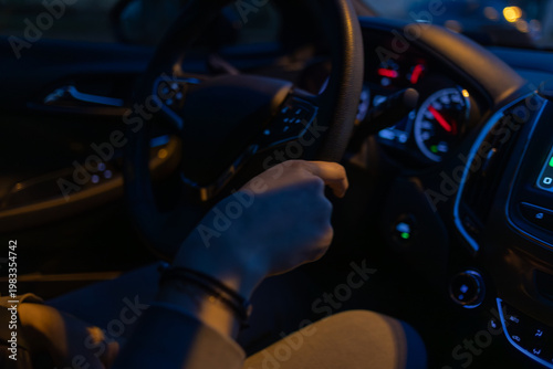 Driver holding steering wheel inside a modern car at night, illuminated dashboard and digital display creating a dynamic urban driving atmosphere with focus on control and technology