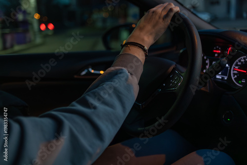 Driver hand on steering wheel at night, illuminated dashboard and city lights creating a dynamic urban driving scene, capturing motion, focus and modern transportation atmosphere