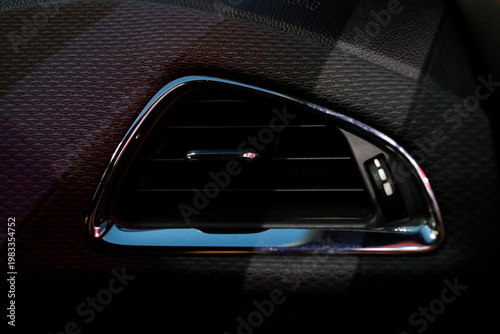 Close-up of a modern car air vent with glossy black and chrome details, soft lighting highlighting textures and design, creating a sleek, high-end automotive interior aesthetic