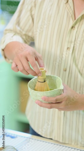 Close up of man whisking matcha tea with bamboo chasen in home kitchen.