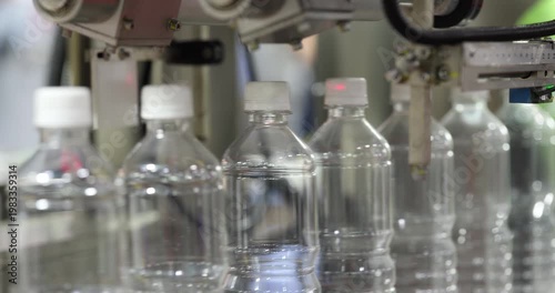 Close up of empty plastic bottles moving along automated conveyor in factory. Packaging production line with modern machinery used in beverage or liquid industry manufacturing.