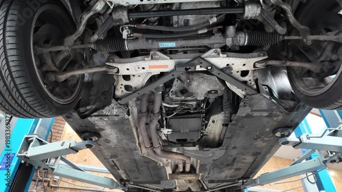 Bottom of a car suspended on a car lift at the garage. Tilt shot. 