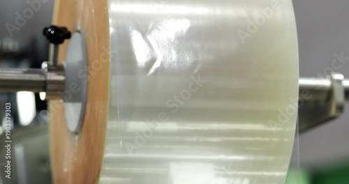 Transparent plastic film roll rotating on industrial machine, flexible packaging material unwinding smoothly in modern production process and manufacturing system, concept of packaging industry