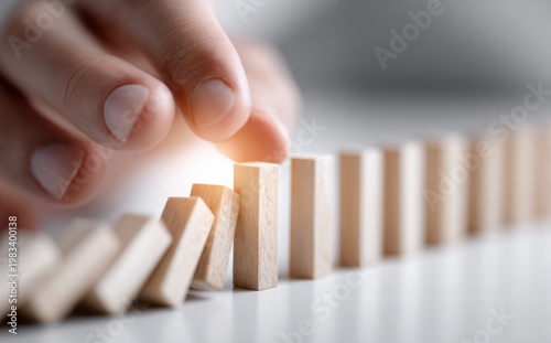Domino Effect: A hand initiates the domino effect by nudging a single wooden piece, setting off a chain reaction and symbolizing cause and effect. 