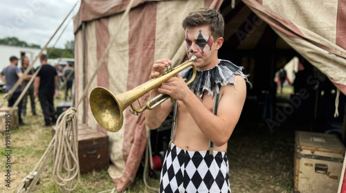 Clown playing trumpet outside circus tent. Man in pierrot costume performing with brass instrument. Professional entertainer with face paint for public event. Artistic circus show concept.
