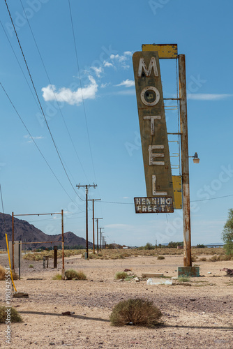 Bild auf Leinwand A weathered and deteriorating vintage roadside motel sign stands in an arid desert landscape under a blue sky with scattered white clouds
