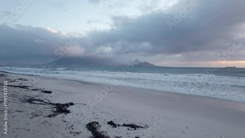 Aerial Drone Shot of Bloubergstrand Beach at Sunset, Panoramic View Across Table Bay toward Table Mountain and Cape Town City Skyline with Blue Moody Clouds