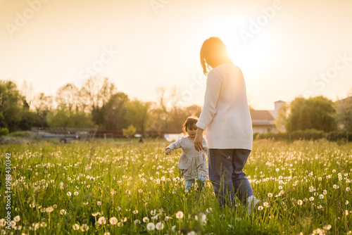 Mother and daughter during an outdoor walk in nature in meadow with flowers, smiling and bonding, concept of motherhood and mother's day
