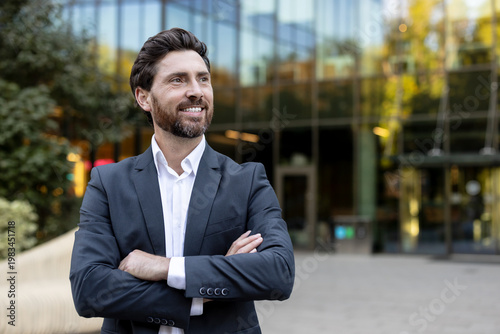 Confident businessman standing outdoors, looking away and smiling, portraying success, leadership, and a positive future with an urban office building background