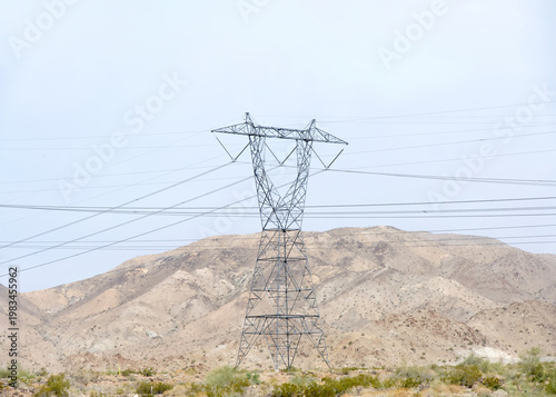 Large tall power lines running through desert landscape with mountains in the background. Hazy skies.