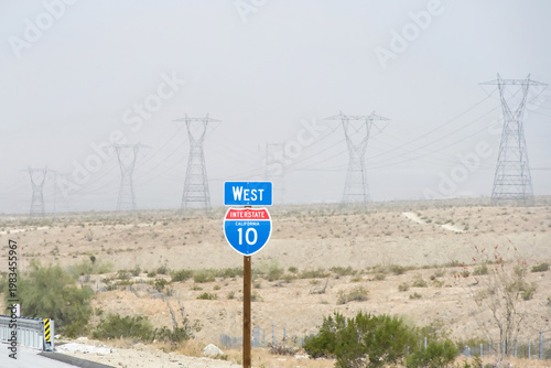 West highway 10 sign on the side of the interstate, row of tall power lines in the background, desert landscape of Southern California.
