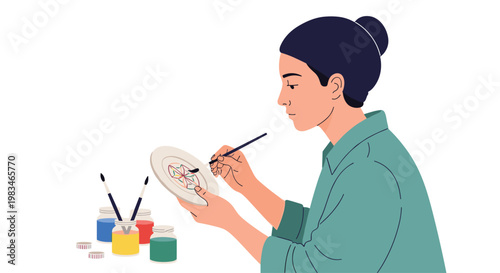 A focused young woman with her hair in a bun meticulously paints a colorful geometric mandala design onto a ceramic plate using a fine tipped art brush.