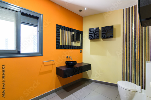 Modern bathroom interior featuring a sleek black basin and vibrant orange wall design