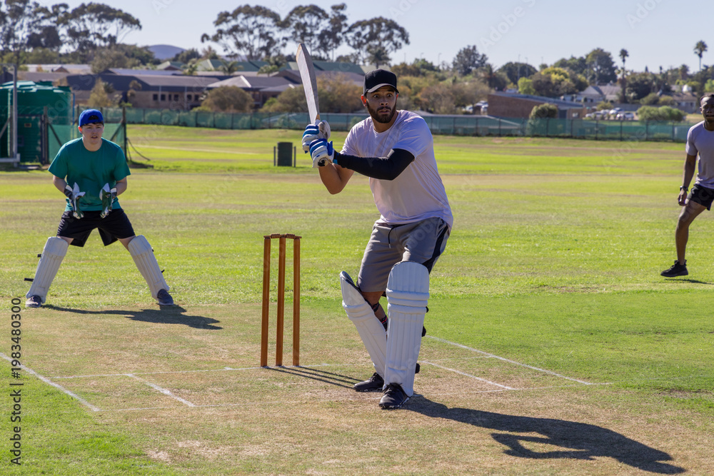 Obraz premium Diverse teammates batting and fielding on suburban cricket pitch, bats, pads, nets visible