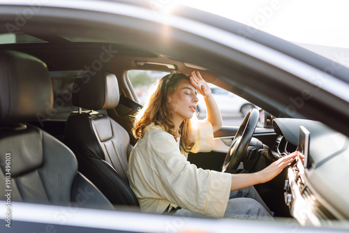Photography Woman sits behind wheel of car, placing hand on forehead, checking airflow