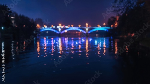 Blue illuminated bridge spanning across a calm river at night with colorful lights reflecting on the water surface slowly