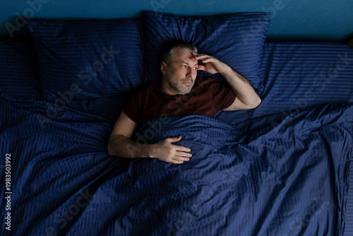 Konstfotografi Man lying in bed holding head with hand, insomnia or stress concept