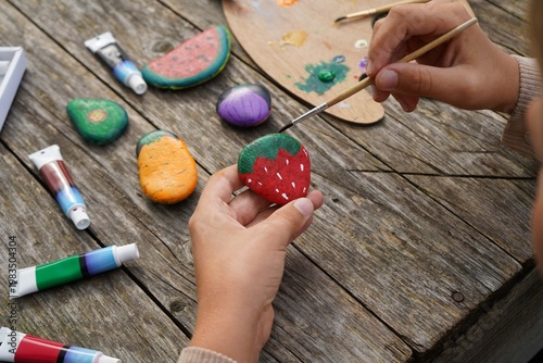 Process of painting fruits and vegetables on flat stones. A boy using brushes and colorful paints.