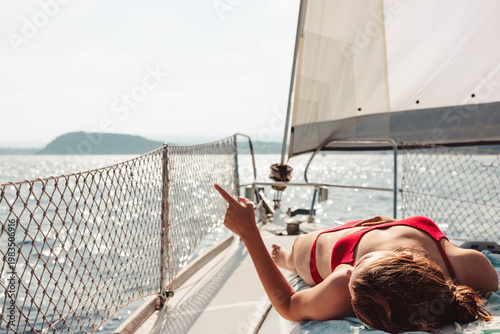 Slika na platnu Woman relaxing on sailboat pointing at distant view
