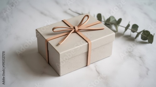 Elegant light beige gift box with orange ribbon on white marble surface