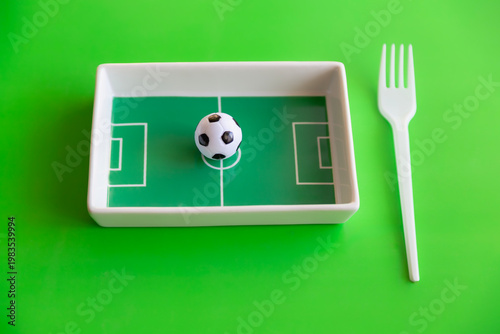 Small soccer ball on football field plate with fork on bright green sports nutrition concept.