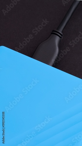 A close-up of a blue external hard drive with a black USB cable connected to it. Black background.