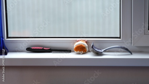 Pet grooming tools and a small toy placed on a white windowsill.