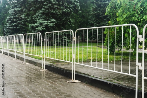 Foto Temporary street fencing installed near a curb on a rainy day with lush trees and wet pavement in the background