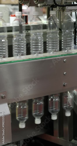 Plastic bottles transition from upright to inverted position on conveyor inside bottling machine. Automated handling stage ensuring precise orientation in production line. Vertical video.