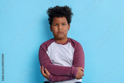 Foto Portrait of resentful little boy with crossed arms on light blue background