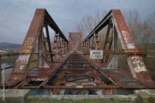 Photos An old steel truss bridge stands abandoned and heavily rusted, marked by a Bridge Closed sign at its entrance