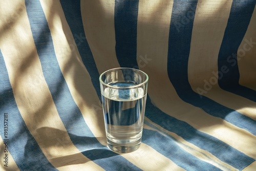 Simple Glass of Water Resting on Blue and White Striped Fabric With Soft Shadows