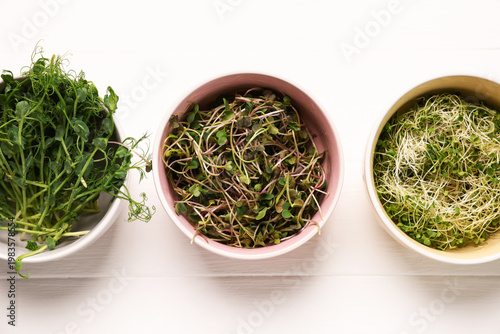Different types of microgreens on white tiled table, flat lay