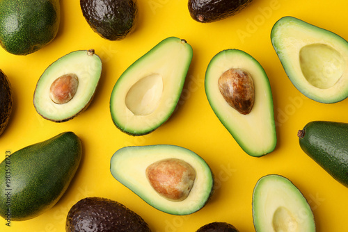 Whole and cut fresh avocados on yellow background, flat lay