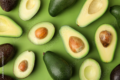 Whole and cut fresh avocados on green background, flat lay