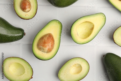 Whole and cut fresh avocados on white tiled table, flat lay