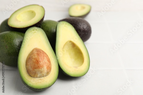 Whole and cut fresh avocados on white tiled table, closeup. Space for text