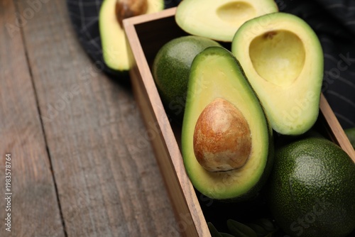 Whole and cut fresh avocados in crate on wooden table, closeup. Space for text