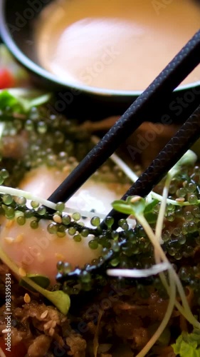 Cutting egg yolk with chopsticks in salad center Asian cuisine runny yolk close-up black plate gourmet food moment Asian seaweed salad with fish and microgreens on black plate gourmet healthy seafood