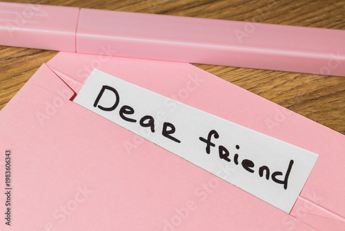 Slika na platnu Pink envelope with a white note that reads dear friend on a wooden table with a
