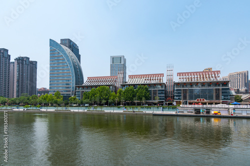 The Hai River flows through the heart of Tianjin, flanked by a mix of modern skyscrapers and green riverside promenades reflecting in the calm water. China, 22 May 2025