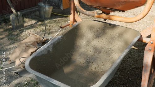 Working process of mixing concrete for the foundation of a private house, cement mortar is poured from a concrete mixer into a wheelbarrow.