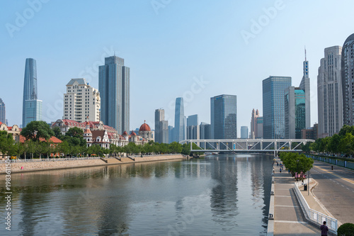 The Hai River flows through the heart of Tianjin, flanked by a mix of modern skyscrapers and green riverside promenades reflecting in the calm water. China, 22 May 2025