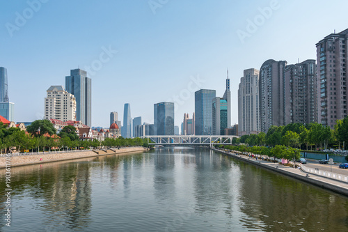 The Hai River flows through the heart of Tianjin, flanked by a mix of modern skyscrapers and green riverside promenades reflecting in the calm water. China, 22 May 2025