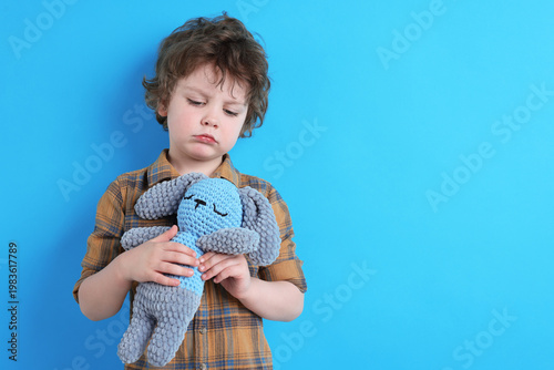 Photos Sad little boy hugging plush toy rabbit on light blue background