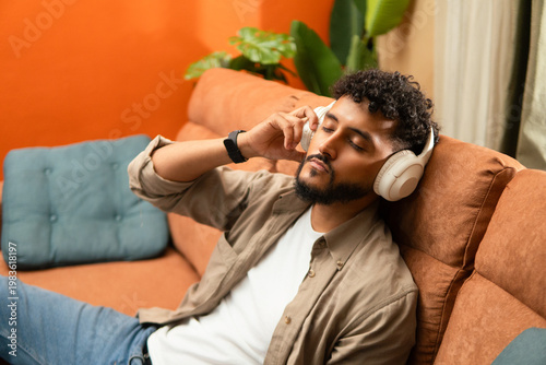 Serene hispanic man lying on sofa wear headphones