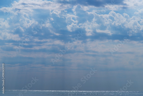 A tranquil ocean scene with a distant sailboat beneath layered clouds and gen...