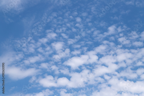 Bright blue sky filled with scattered white clouds forming a soft, textured c...