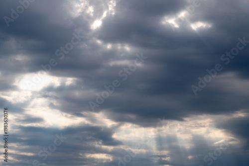 Dramatic overcast sky with sun rays piercing through thick clouds, creating m...